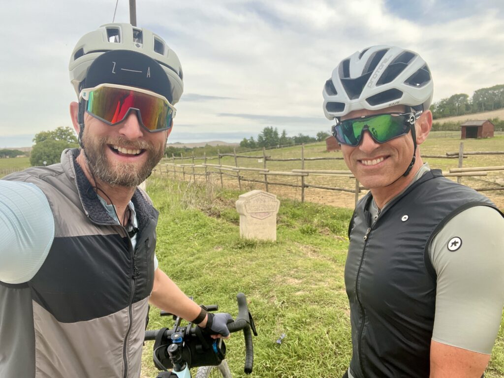 Two cyclists pose for a selfie at the start of a Strade Bianche gravel segment 